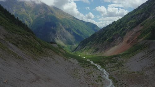 Aerial View of a Mountain Stream Flowing Between Cloudcovered Mountain Peaks