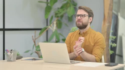 Man Massaging Wrist While Working on Laptop