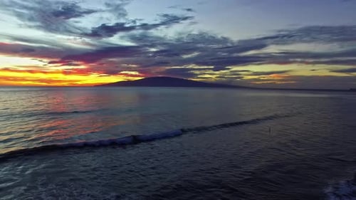 Sunset over the Pacific ocean and Hawaiian landscape with gentle waves on the beach
