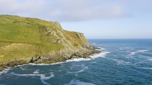 Rocky Coastal Formations And Lush Green Hills With Waves Crashing The Shoreline