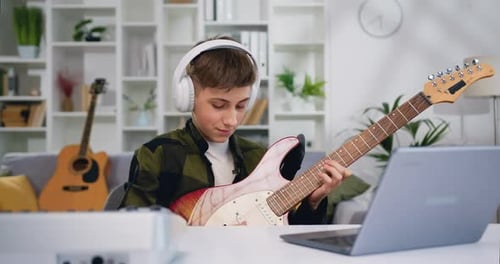 Teen Guitarist Plays While Using Laptop