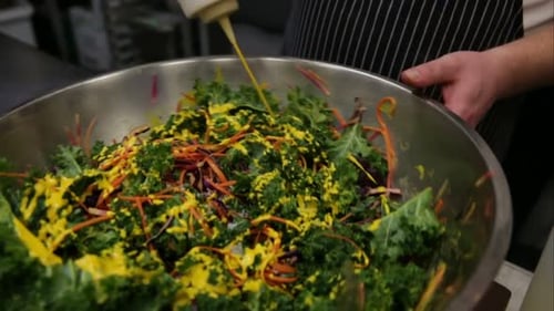 Chef pouring mustard sauce dressing on fresh kale salad in restaurant kitchen
