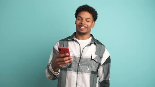 Smiling Young Man Using Smartphone in Blue Studio