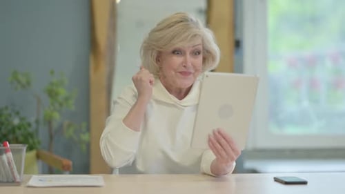 Senior Woman Celebrates with a Tablet Indoors