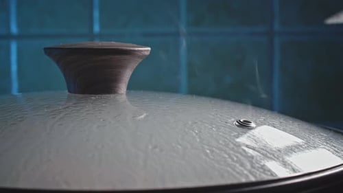 Close up of cooking pot gently releasing steam through venting hole on glass lid