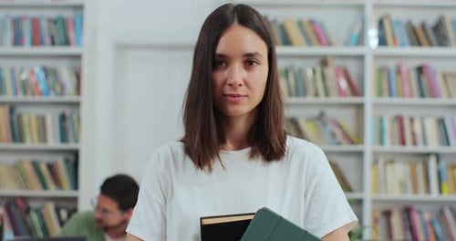 Close Up Portrait of Beautiful Young Girl Holding Book and Digital Tablet in Library Bookshelf