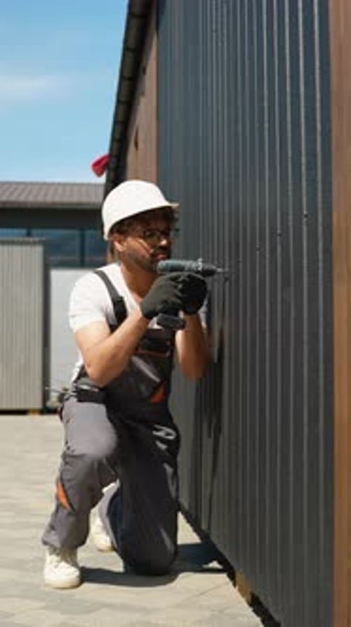 Construction Worker Using Cordless Drill on Metal Siding