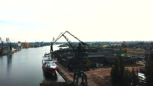 Drone flying around cranes and cargo ships in the shipyard docks