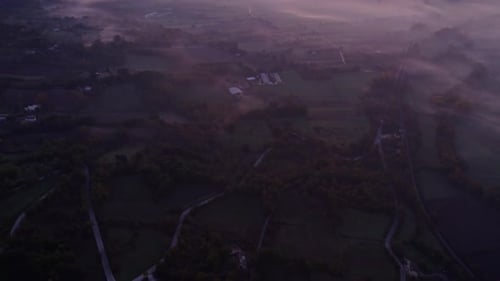 Aerial view of foggy morning countryside with fields, road, and mountain, Italy.