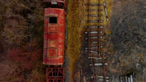 Birds-eye drone footage looking straight down onto derelict, heavily rusted red train carriages