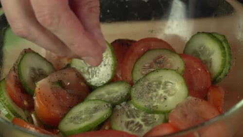 Hands of middle man european pours ground black pepper on sliced vegetables tomatoes and cucumber