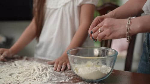 Cook at Home Mom and Daughter are Cooking Mom Breaks an Egg Into a Glass Bowl with Flour