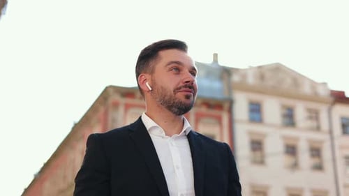 Close Up of Caucasian Bearded Businessman Standing on Street and Putting Headphones at His Ears