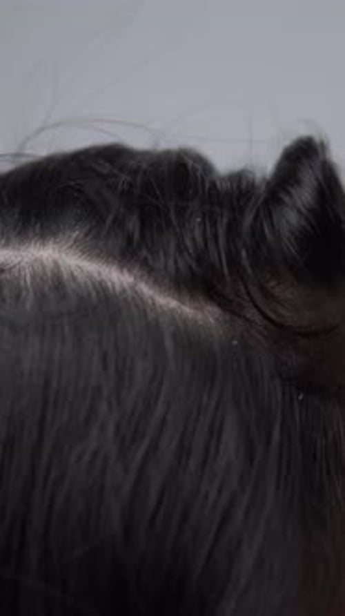 Close up footage of a young Asian woman pointing to the dandruff on her hair.