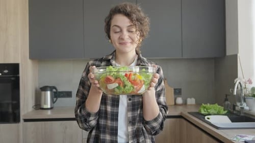 Woman Holds Bowl of Fresh Salad in Kitchen