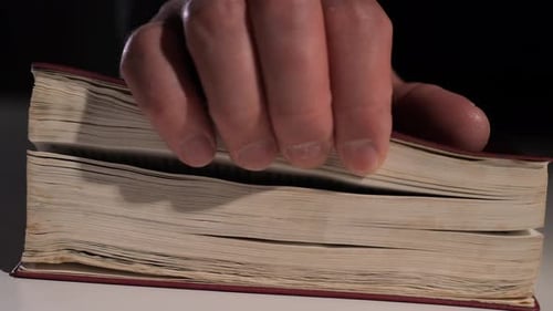 Hand Closing Old Book Gently on White Table in Dark Room
