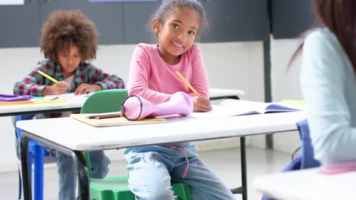 In school, smiling girl writing in notebook at classroom desk, enjoying learning
