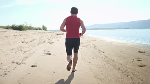 Man runs on a beach. Young sportive man runs barefoot on a sandy coast along the river