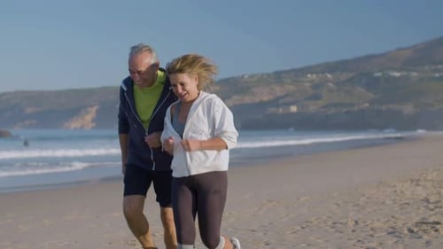 Cheerful Man and Woman Jogging Along Ocean Coast on Summer Day