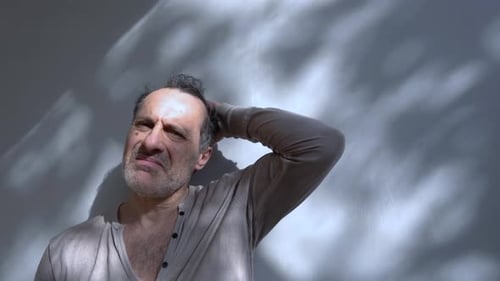 Distressed Man Rubs Face Against Sunny Wall