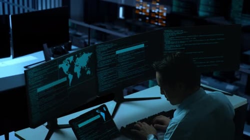 Asiatischer Mann arbeitet mit Tablet, während er Code mit mehreren Computerbildschirmen im Büro schreibt