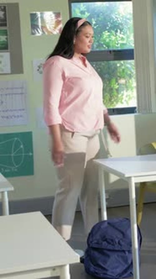 Vertical video: Walking teacher in pink shirt entering class passing blue backpack prepping lesson