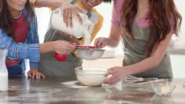 Women friends baking together in kitchen, sifting flour into mixing ...