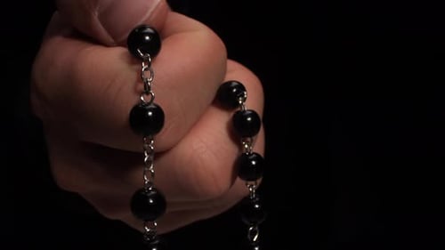 Hand holding rosary beads in dark setting