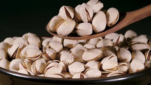 Dried Pistachio Nuts with Cracked Shells and Green Kernels Falling into a Rustic Ceramic Bowl