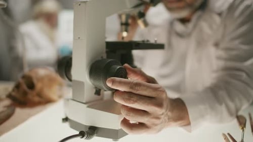 Close-Up of Archaeologist Adjusting Microscope Focus in Research Laboratory