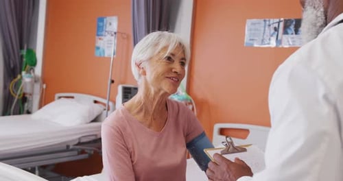 African american male doctor taking blood pressure of senior caucasian female patient at hospital