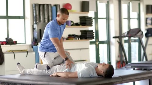 Assisting man with leg exercises, physical therapist in rehabilitation center