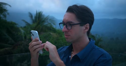Man Holding Phone Surrounded by Tropical Nature