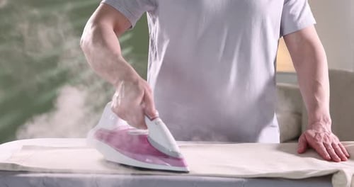 Man ironing pants on board at home, closeup. Camera moving