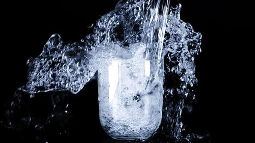 A jet of water is poured into glass goblets on a black background and creates a splash of water