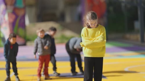 Niña acosada de pie sola en el patio de la escuela