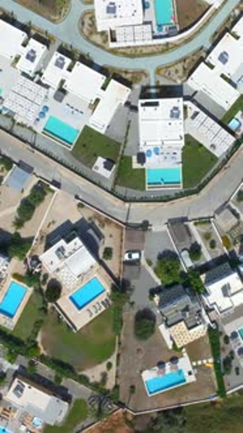 Vertical drone shot over holiday homes with pools on top of a hill in Greece