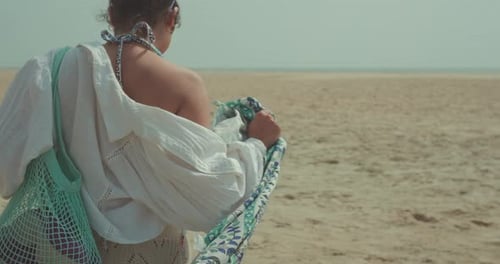 Woman carrying beach bag walking on sand
