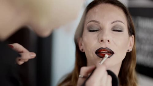 Professional Makeup Artist Applying Lipstick on Lips of Middleaged Lady Model in Beauty Studio
