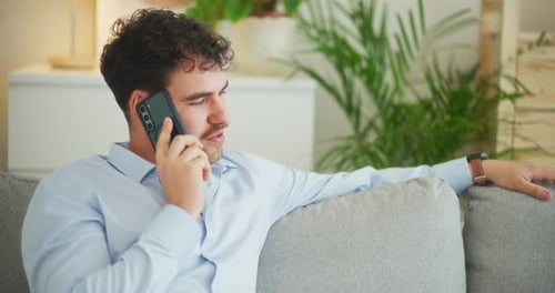 Man Sits on Sofa and Talks on Cell Phone