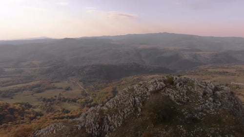 Tracking out aerial shot over rocky hill, valley and forest as background