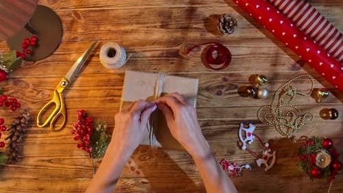 Hands Decorating Christmas Gift with Twine and Berries