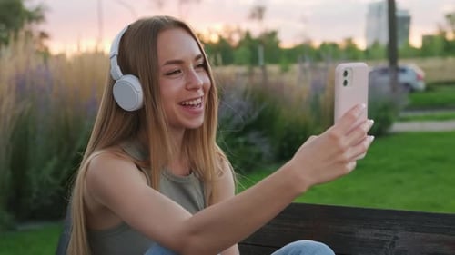 Young Woman Talks to Friend on Phone Sitting on Park Bench