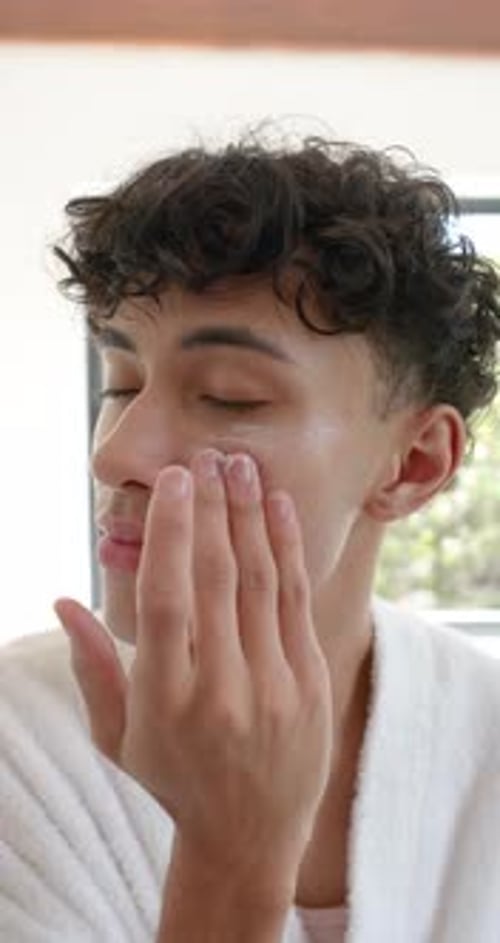 Man Applying Lotion to Face in Bathroom