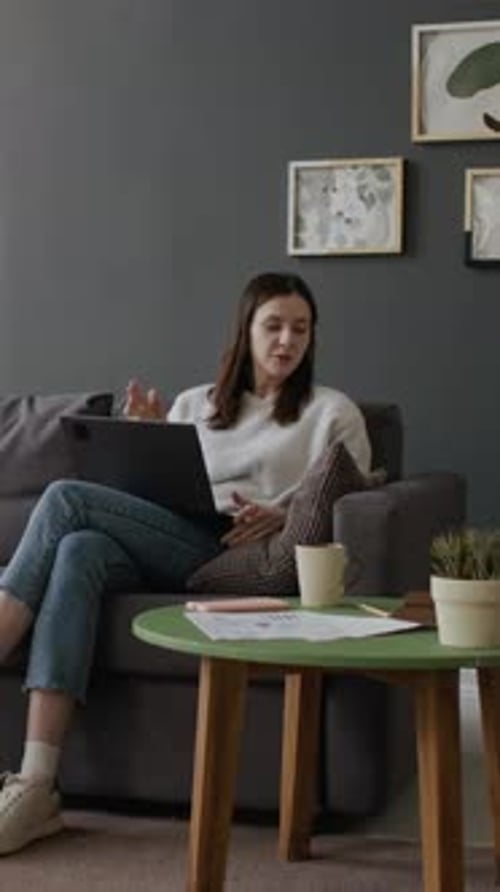 Woman on Couch Attending Virtual Meeting with Laptop
