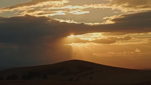 Cross on hill Sun rays slowly appear from behind clouds Silhouette