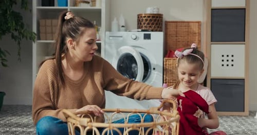Junge Mutter und Tochter sitzen im Badezimmer auf dem Boden und sortieren Kleidung