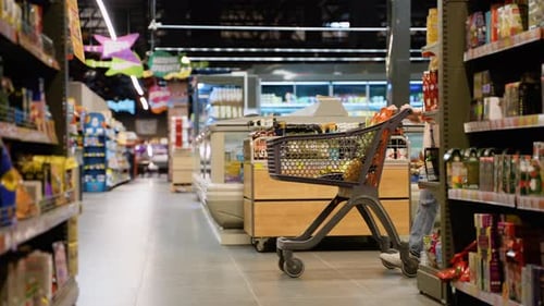A Woman Shopper Confidently Pushes a Cart Overflowing with Fresh Groceries in Supermarket