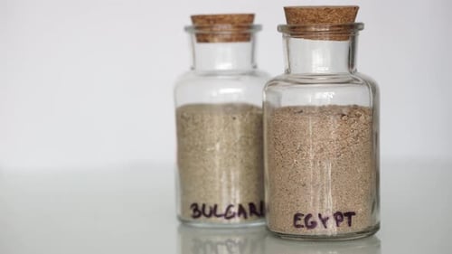 Mão de homem caucasiano colocando pequenos frascos transparentes cheios de areia de diferentes países em seguida