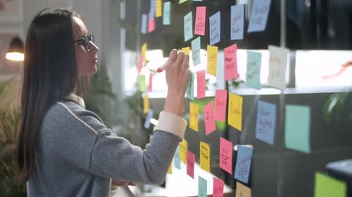 Woman Brainstorming with Sticky Notes on Glass Wall